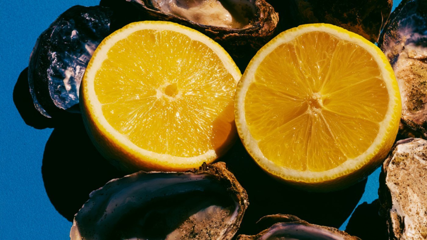 Two orange halves resting on oyster shells against a bright blue background